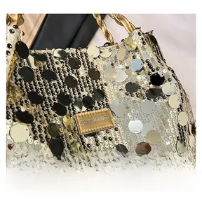 Close-up of golden sequins on a large tote bag with a metal knot handle and logo plaque