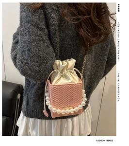 Detail of pink woven bucket bag featuring pearl handle and gold chain strap on model
