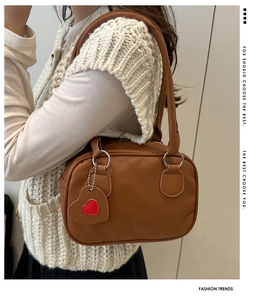 Detail of a brown lychee pattern leather handbag with a heart-shaped tag and silver rings