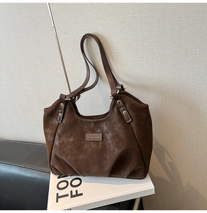 Detail of dark coffee suede shoulder bag featuring a leather logo tag and gold rivets