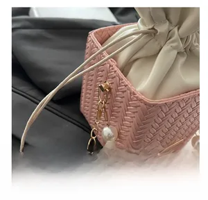 Detail of pink woven bucket bag featuring gold metal hooks and luxury oversized pearl chain