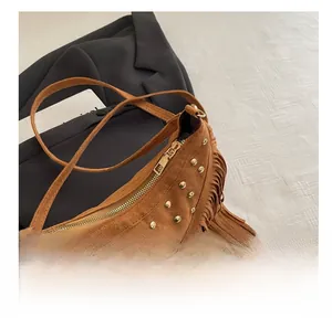 Dettaglio borsa scamosciata marrone con borchie dorate e nappe in stile boho