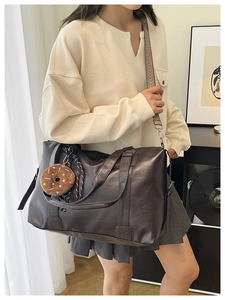 Detail of dark brown leather pillow bag with wide woven strap and plush charm