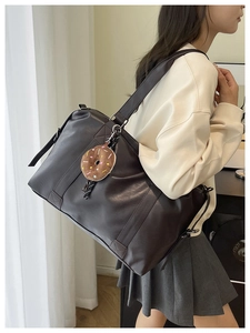 Détail du sac polochon en similicuir marron avec bandoulière large et breloque donut