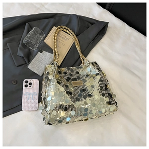Detail der Pailletten-Tasche mit Metallgriffen und Logo-Plakette auf schickem Hintergrund