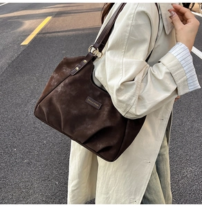 Close-up of brown suede tote bag featuring front pleats and gold metal ring strap hardware