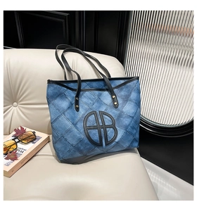 Close-up of quilted blue denim tote bag with black leather AB logo on beige sofa
