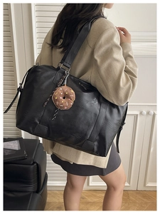 Close-up of black leather travel tote bag with brown donut plush charm and wide strap