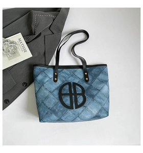 Flat lay of tote bag with blue denim texture, black logo, and gold metal rivets