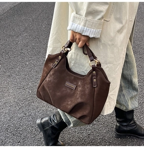 Macro detail of brown suede tote bag featuring side leather straps and gold metal ring