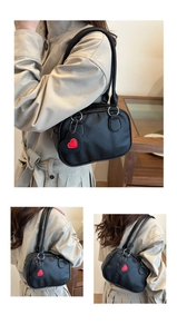 Detail of black pebbled leather handbag featuring a decorative red heart charm and straps