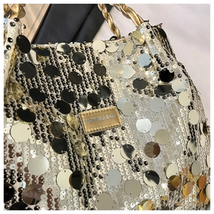 Detail der Pailletten-Schultertasche mit goldenem Kordelgriff und Metall-Markenplakette