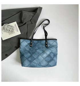 Detailed view of blue denim quilted tote bag with black straps on a blazer backdrop