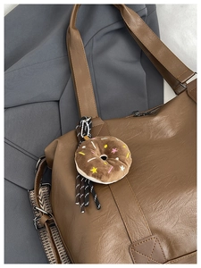 Detailed view of brown leather tote bag with donut plush charm and checkered woven strap