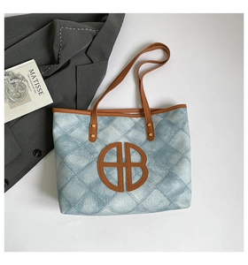 Detail of light blue quilted tote bag with brown leather accents and circular logo