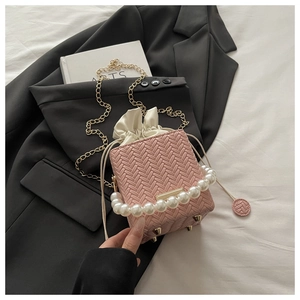 Detailed top view of pink woven bucket bag with pearl handle and golden bottom studs