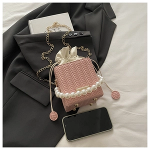 Top view of pink woven bucket bag with pearl handle and golden chain on white sheet