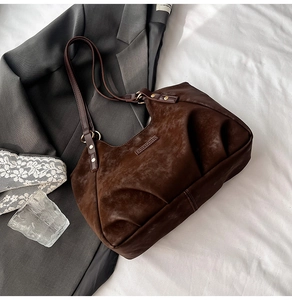 Detailed close-up of dark brown suede shoulder bag with gold rivets and pleats