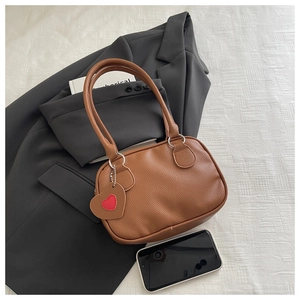 Gros plan sur le sac à main marron en cuir grainé avec pendentif cœur et poignées