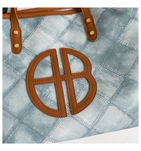 Detailed shot of denim tote bag with quilted pattern, brown leather logo, and gold rivets