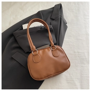 Détail du sac à main marron en cuir grainé avec anneaux argentés sur blazer noir