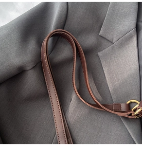 Close-up of deep brown leather shoulder strap with white contrast stitching and gold buckle