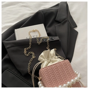 Pink woven mini bucket bag with pearl handle and metal chain on a black blazer
