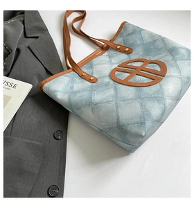 Detail of denim quilted tote bag with brown leather logo and gold rivet handles
