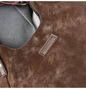 Detailed close-up of dark brown suede shoulder bag featuring a stitched leather logo tag