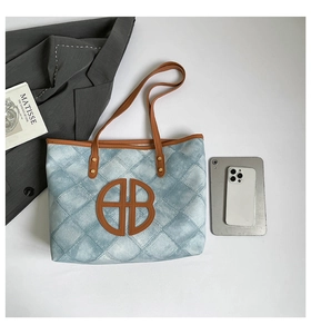 Detail of blue denim tote bag with quilted pattern, leather HB logo and large capacity