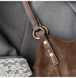 Macro shot of gold metal ring hardware and fine stitching on brown suede tote bag