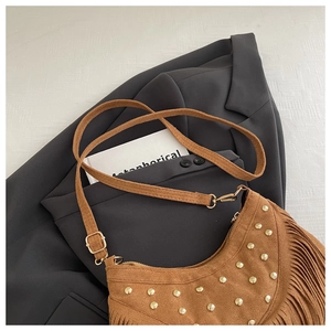 Detailed view of a brown suede hobo bag with gold rivets and fringes on a grey blazer