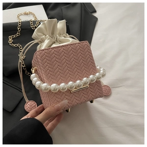 Detail of pink woven bucket bag with pearl handle and golden chain shoulder strap