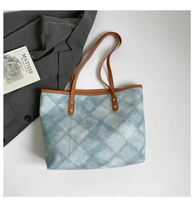 Close-up of blue denim quilted tote bag with brown leather handles and gold rivets