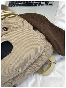 Close-up of corduroy puppy backpack featuring 3D ears and colorful striped scarf detail