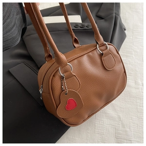 Détail d'un sac à main marron avec pendentif cœur rouge et finitions métalliques argentées