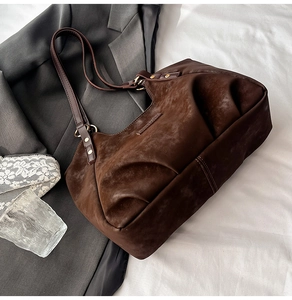 Detailed view of dark brown suede tote bag with pleated texture and gold rivets