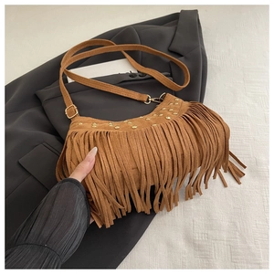 Detail of brown suede crossbody bag with fringe, gold studs, and thin shoulder strap