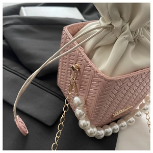 Detail view of a pink woven bucket bag featuring pearl handles and gold chain strap