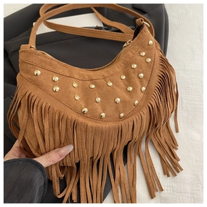 Detail view of brown suede crescent bag featuring gold rivets and long fringe tassels
