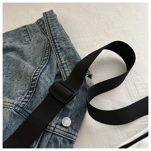 Detail of blue denim chest bag featuring a JEANS engraved button and adjustable strap