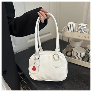 Close-up of white lychee pattern handbag featuring a red heart pendant and silver chain