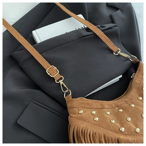Detailed close-up of brown suede shoulder bag with gold metal rivets and bohemian tassels