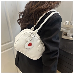 Détail d'un sac à bandoulière en cuir grainé blanc avec un charm en forme de cœur rouge
