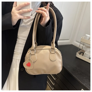 Detail view of beige lychee grain leather handbag with red heart charm accessory
