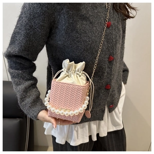 Close-up of pink woven bucket bag with pearl handle and golden chain strap on model