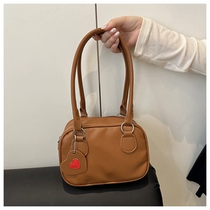 Dettaglio borsa vintage marrone con trama litchi, anelli argento e pendente a cuore