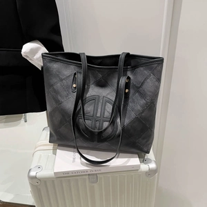 Quilted black denim tote bag with circular logo displayed on a white suitcase