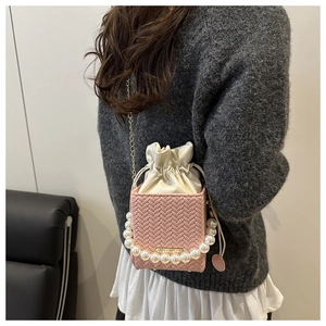 Detail of pink woven bucket bag with elegant pearl handle and gold chain strap