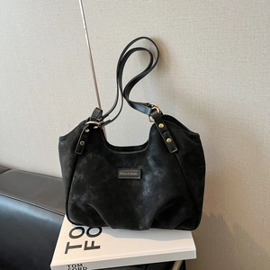 Minimalist black faux suede shoulder bag with gold hardware on a stack of books